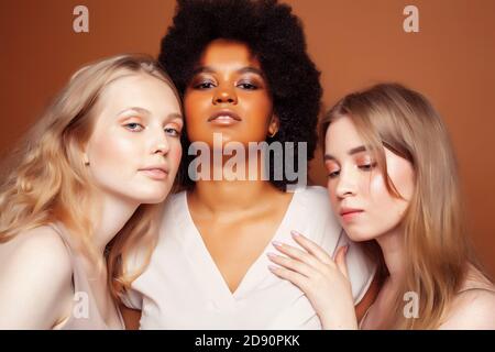 Junge hübsche kaukasische, afro, skandinavische Frau posiert fröhlich zusammen auf braunem Hintergrund, Lifestyle diverse Nationalität Menschen Konzept Stockfoto