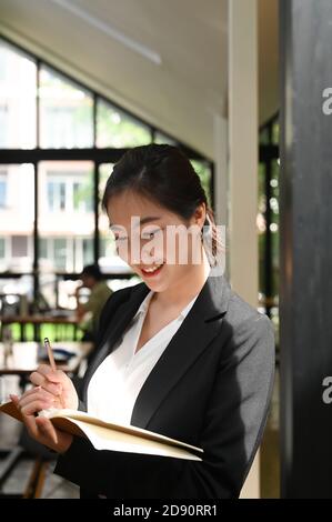 Portrait einer attraktiven jungen Geschäftsfrau, die auf einem Notizblock schreibt und im Besprechungsraum steht. Stockfoto