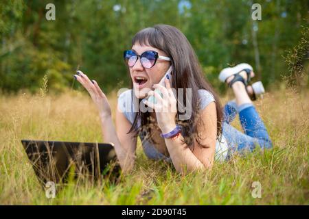 Junge Frau, die vor dem Laptop am Telefon emotional spricht. Stockfoto