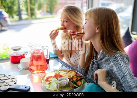 Fröhliche kaukasische Freunde verbringen Zeit zusammen in hellen gemütlichen Zeit Café, sie haben Spaß, reden, chatten. Mittagessen oder sie feiern etwas, unterhaltsam Stockfoto