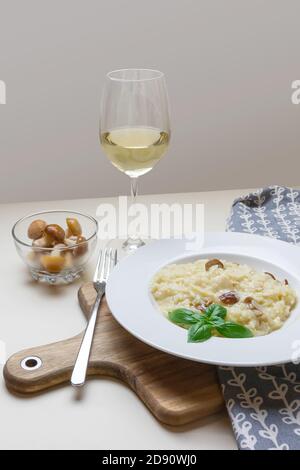 Vegetarisches Gourmet-Pilz-Risotto auf weißem Teller, gelber Hintergrund, serviert mit einem Glas Weißwein. Eine norditalienische Reisgericht mit Brühe gekocht, bis es eine cremige Konsistenz erreicht. Stockfoto