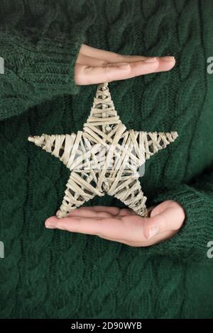 Weibliche Hände halten eco weihnachtsstern. Teenager-Mädchen tragen tiefgrünen Pullover und halten Sterne Dekoration. Neujahr und weihnachtskonzept. Vertikale Größe, selektive Fokus Stockfoto