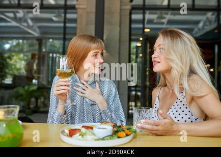 Zwei junge und schöne Freundinnen sitzen reden, teilen Nachrichten im Restaurant. Attraktive Frauen verbringen Mittagessen im Café, haben Gespräch, Gespräch Stockfoto