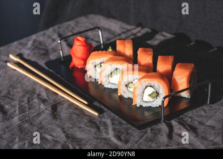 Sushi-Rolle mit Essstäbchen auf einem Holzständer auf einem schwarzen Ständer. Sushi-Menü. Stockfoto