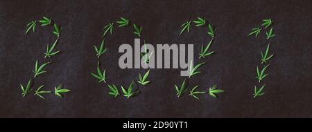 Muster von Cannabisblättern in Form von Zahlen 2021 auf dunklem Hintergrund. Das Konzept eines neuen Jahres. Hintergrund der Cannabispflanze. Speicherplatz kopieren. Der Stockfoto