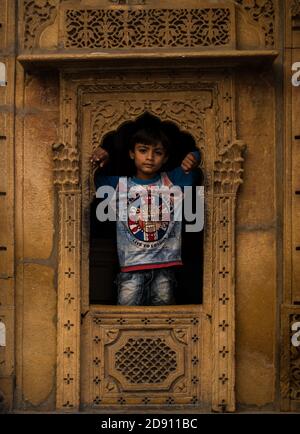 Jaisalmer, Rajasthan / Indien - november 02 2020 : kleiner Junge, der durch ein Fenster aus seinem Haus guckt Stockfoto