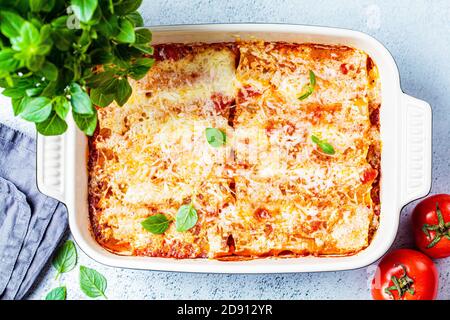 Traditionelle Cannelloni mit Fleisch, Tomatensauce und Käse in einer Backform, grauer Hintergrund. Konzept der italienischen Küche. Stockfoto