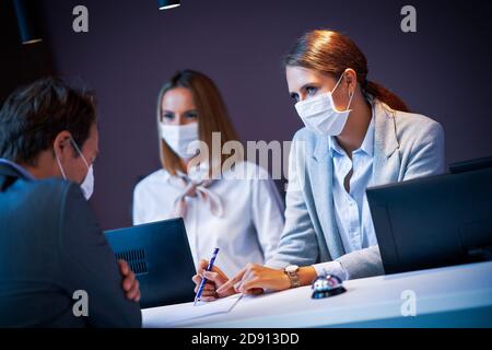 Geschäftsmann in Maske an der Rezeption eines Hotel-Check Zoll Stockfoto