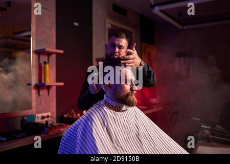 Friseuse beim Friseur, im Salon. Barbier männlich schneidet die Haare auf dem hübschen jungen Client den Kopf, den Prozess der Erstellung von Frisuren für Männer von professionellen Stockfoto