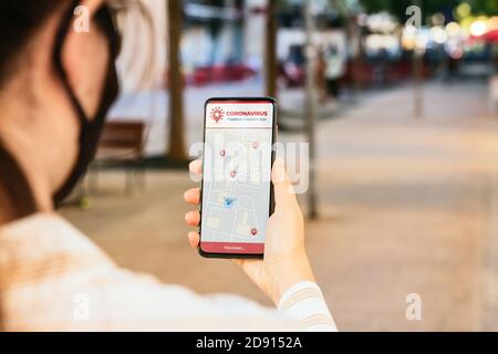 Stock Foto von einer jungen Frau mit einer Coronavirus Tracking-App in ihrem Handy, während auf der Straße. Die Standorte der infizierten Personen erscheinen auf dem Skre Stockfoto