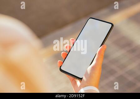 Handy-Mockup von einer Frau Hand gehalten, die auf der Straße ist. Mobiltelefon mit weißem Bildschirm, um ein Design einzufügen. Vorlage Stockfoto