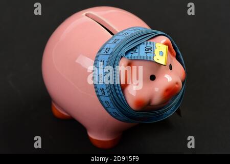 Maßband um Sparschwein oder Geldschachtel auf schwarzem Hintergrund gewickelt. Sparungen und Finanzian Diät-Konzept Stockfoto