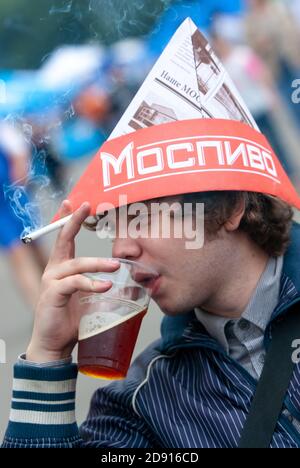 Der junge Mann trinkt Bier aus einem Plastikbecher und raucht auf einem Straßenbierfest eine Zigarette. Moskau, Russland, 09.07.2009 Stockfoto