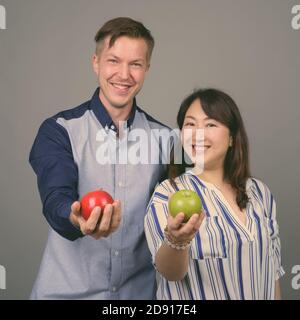 Junge gut aussehende Geschäftsmann und reifen asiatischen Geschäftsfrau vor grauem Hintergrund Stockfoto