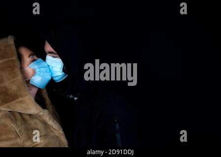 Junges Paar zusammen im Dunkeln mit Winterjacke mit schützenden medizinischen Masken für Covid-19, Romantic und Coronavirus Konzept Stockfoto