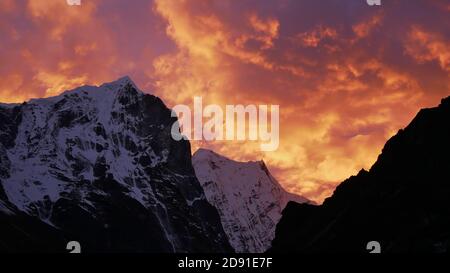 Atemberaubender Sonnenuntergang über eisbedeckten Bergen im Himalaya in der Nähe des Dorfes Thame, Khumbu, Nepal mit einem dramatischen, farbenfrohen Himmel, der wie Feuerflammen aussieht. Stockfoto