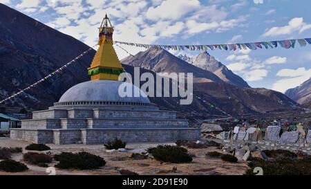 Buddhistische Stupa (religiöses Denkmal) in einem Tal in der Nähe von Thame, Khumbu, Himalaya, Nepal mit Gebetsfahnen, die im Wind fliegen, und einer Mauer aus Manikasteinen. Stockfoto