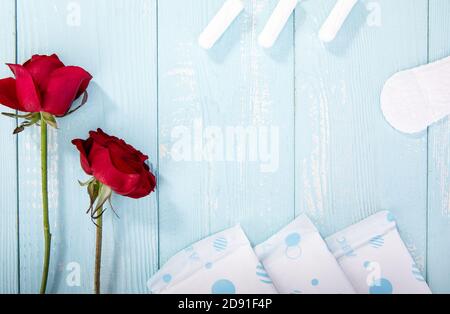 Rosen, Sanitäranlagen und Tampons auf blauem Holzhintergrund mit Platz für Text Stockfoto