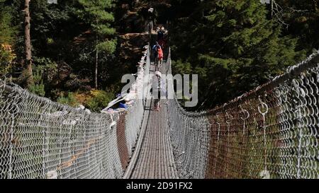 Träger überqueren eine Hängebrücke mit gefesselten buddhistischen Gebetsfahnen, die den Dudhkoshi River in einem Tal in der Nähe von Manjo auf dem Mount Everest Base Camp Trek überspannen. Stockfoto