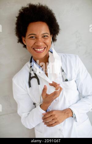 Weibliche afroamerikanische Arzt tragen weiße Uniform und Abheben Gesichtsmaske im Krankenhaus Stockfoto