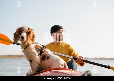 Mann mit Hund im Kanu auf dem See. Junger Rüde mit Spaniel im Kajak-Ruderboot, aktive Freizeit mit Haustieren, Begleitung, Abenteuerhunde Stockfoto