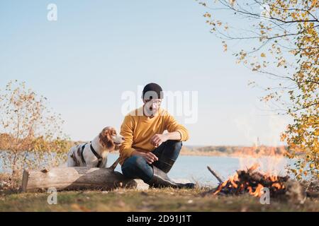 Der Mann umarmt seinen Hund, der am See sitzt. Aktive Erholung mit Haustieren, auf Abenteuer gehen, Gesellschaft: spaniel Hund und sein Besitzer sitzen im Freien Stockfoto