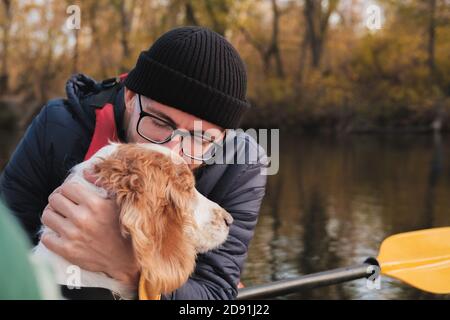 Mann in einem Ruderboot küsst seinen Hund. Gesunde Freundschaft von Mensch und Tier: Person mit seinem Welpen auf einem Boot Abenteuer auf dem Fluss Stockfoto