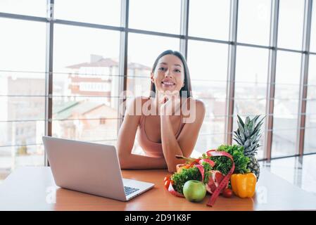 Brunette mit schlanken Körper Typ sitzt am Tisch mit Laptop und gesunde Lebensmittel Stockfoto