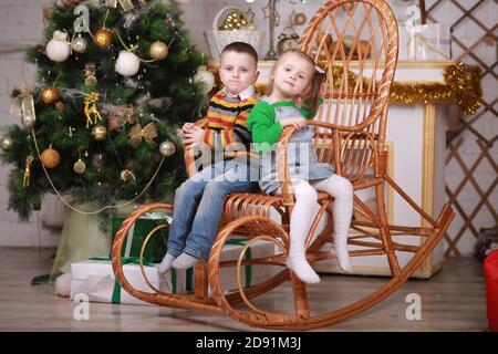 Nettes kleines Mädchen und Junge sitzen in Schaukelstuhl in der Nähe weihnachtsbaum Stockfoto