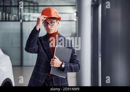 Porträt des jungen Mannes in Schutzhelm und in formell Kleidung, die drinnen steht Stockfoto