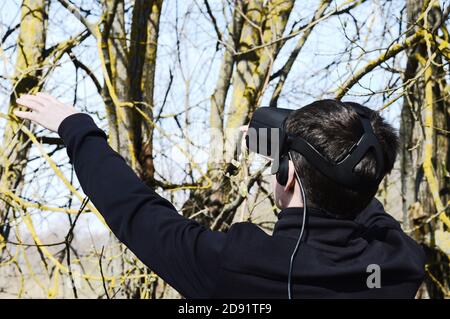 Junger Mann versuchen VR-Brille im Freien und erleben virtuelle Technologien Interagieren Sie mit der tatsächlichen Natur Stockfoto