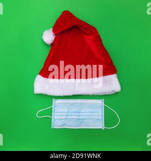 Weihnachtsmann Hut und Gesichtsmaske auf grünem Hintergrund, kreative Minimal Konzept von Weihnachten und Neujahr 2021. Neue normale Feiertage während der Pandemiezeit Stockfoto