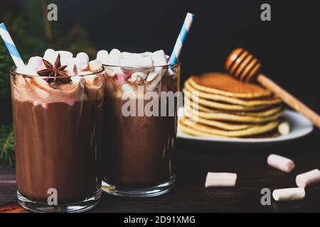 Heiße Schokolade mit Marshmallows und Strohhalmen auf einem Hintergrund Pfannkuchen mit Honig Stockfoto