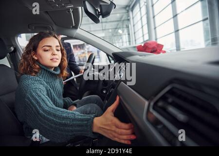 Professionelle Verkäufer Unterstützung junge Mädchen durch die Wahl neuer moderner Automobil drinnen. Frau, die drinnen sitzt Stockfoto