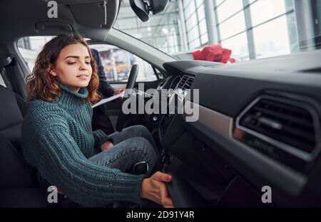 Professionelle Verkäufer Unterstützung junge Mädchen durch die Wahl neuer moderner Automobil drinnen. Frau, die drinnen sitzt Stockfoto