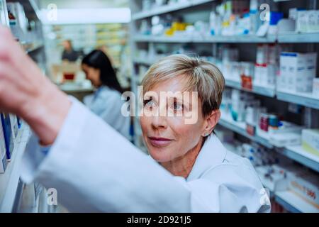 Qualifizierter älterer Apotheker auf der Suche nach verschreibungspflichtigen Medikamenten Boxen stehen In der Insel der Apotheke Stockfoto