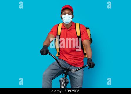 afroamerikanische Lieferung Mann in medizinische Maske Fahrrad fahren Stockfoto