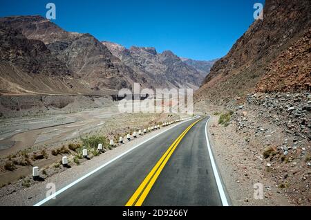 Autobahnstraße in den Anden entlang des Canyonflusses. Leere Straße in aridem Klima als Wüste mit felsigem Gelände. Kurvige Straße mit gelber Trennlinie Stockfoto