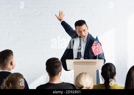 Aufgeregter indischer Agitator, der während des Gesprächs mit den Wählern im Konferenzsaal gestikuliert, verschwommener Vordergrund Stockfoto