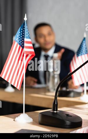 Kleine amerikanische Flagge mit Mikrofon auf Tisch mit verschwommenem indianer Mann im Hintergrund Stockfoto
