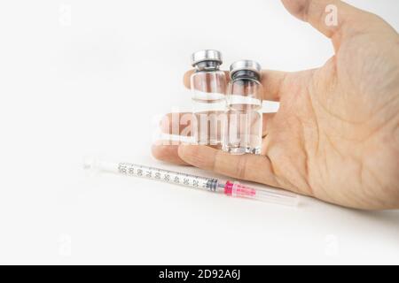 Zwei Fläschchen mit Medizin und Spritze in einer Hand für die Injektionsbehandlung. Covid-19 Impfstoffkonzept. Isoliert auf weißem Hintergrund Stockfoto