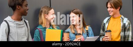 Panorama-Aufnahme lächelnder multiethnischer Teenager mit Notizbüchern und Kaffee In der Nähe des Gebäudes stehen Stockfoto