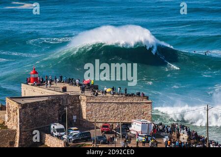 Surfer reiten riesige Welle in der Nähe des Leuchtturms in Nazare, Portugal. Nazare ist bei Surfern bekannt dafür, dass sie die größten Wellen der Welt haben. Stockfoto