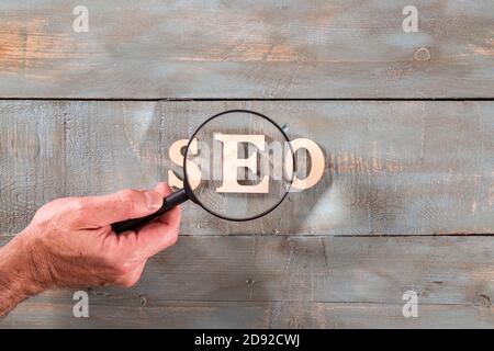 Mann, der durch Lupe ein seo Wort mit weißen Buchstaben gebildet. Konzept zur Suchmaschinenoptimierung. Stockfoto