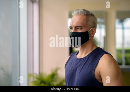 Reifer persischer Mann mit Maske Denken während soziale Distanzierung an Der Fitnessraum Stockfoto