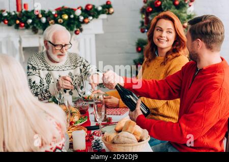 Selektiver Fokus der Frau, die auf den Mann schaut, der die Champagnerflasche öffnet In der Nähe von Verwandten Stockfoto