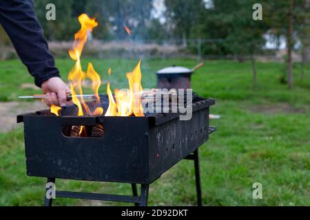 Das Fleisch wird auf dem Grill, Brazier gekocht. Nahaufnahme Mann die Hand dreht Fleisch auf dem Gitter über dem Feuer. Kochen im Freien. Treffen mit Freunden, Picknick, wir Stockfoto