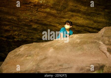 Ein Junge, der Gesichtsmasken trägt, steht über einem großen Felsen In einer Sandsteinschlucht Stockfoto