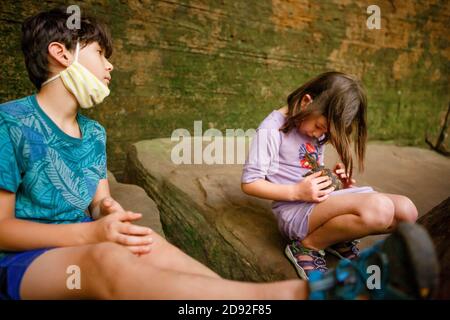 Zwei Kinder sitzen in einer felsigen Schlucht und spielen mit einem Kleine gemalte Schildkröte Stockfoto