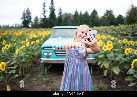 Tween Girl Holding Telefon unter Selfie in Sonnenblume Feld mit Lkw Stockfoto